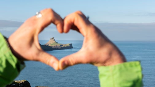 Worm's Head peeping through heart-shaped hand gesture at Rhosili
